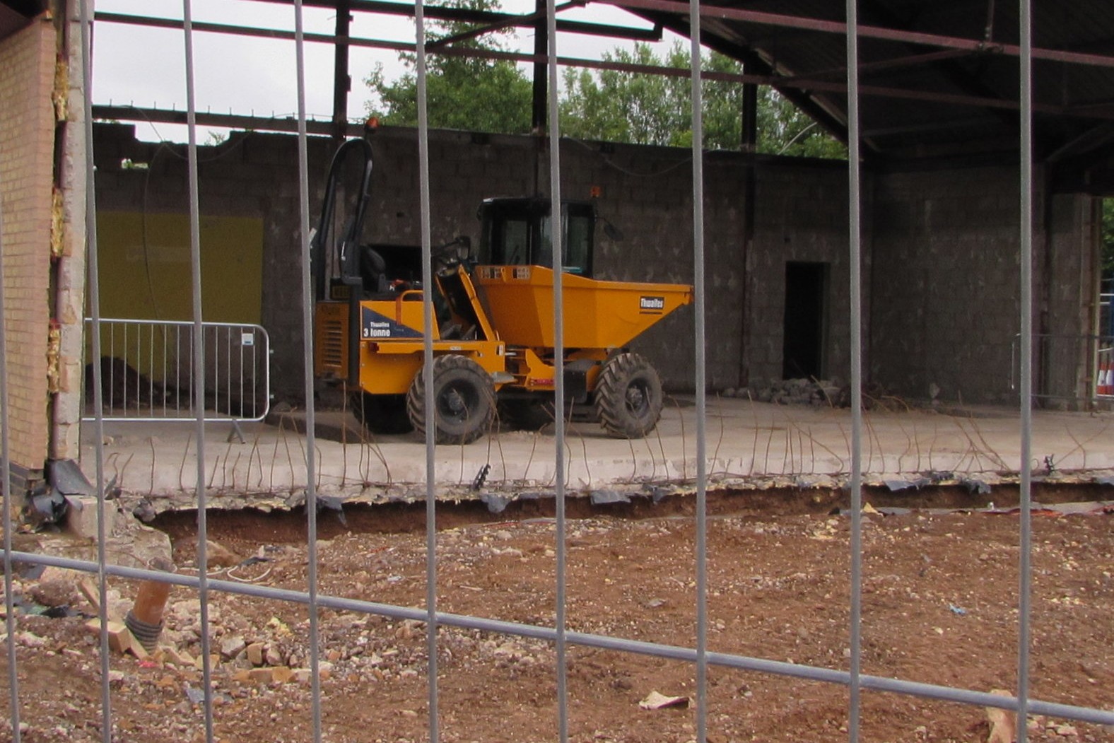 Yellow site dumper parked behind steel mesh fencing on a building site